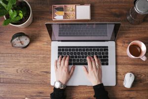 Woman’s hands working on laptop at home office, top view